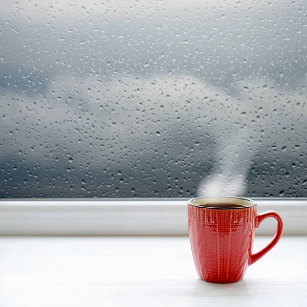 Cup of coffee on a windowsill. In the background window with raindrops and clouds — Stock Photo, Image