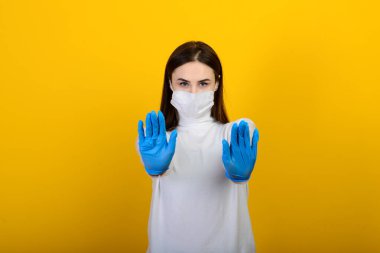 Tıbbi eldivenli bir kız beyaz arka planda tıbbi bir maske takıyor. Solunum hastalığı. Covid 19