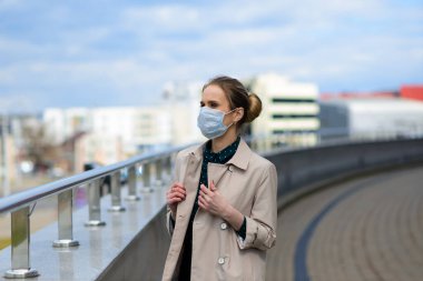 Maske takan ve şehirde telefonla konuşan genç bir iş kadını.