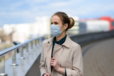 Maske takan ve şehirde telefonla konuşan genç bir iş kadını.