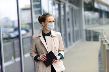 Maske takan ve şehirde telefonla konuşan genç bir iş kadını.