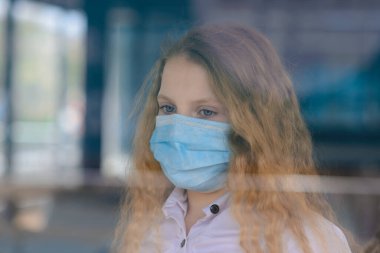 Kapalı oyun parkında yüzü maskeli, üzgün, beyaz bir çocuğun portresi. Coronavirus sosyal mesafesi.