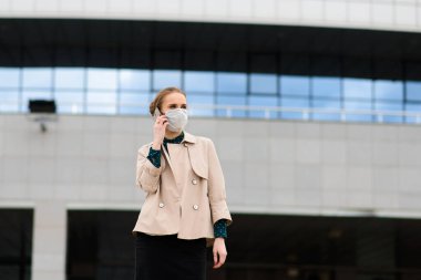 Maske takan ve şehirde telefonla konuşan genç bir iş kadını.