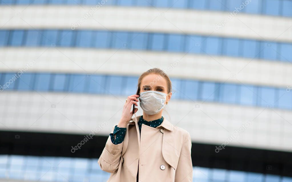 A young businesswoman wearing a mask and talking on the phone in the city