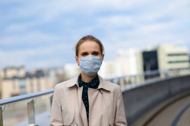 Maske takan ve şehirde telefonla konuşan genç bir iş kadını.
