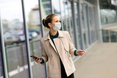 Maske takan ve şehirde telefonla konuşan genç bir iş kadını.
