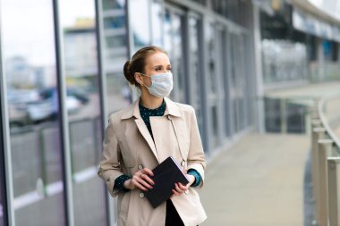 Maske takan ve şehirde telefonla konuşan genç bir iş kadını.