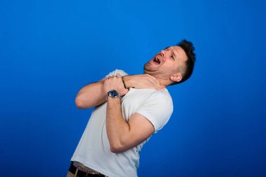 Mavi stüdyo arka planında duran ve gülümseyen yakışıklı bir adam. Yarım boy erkek portresi. İnsan duyguları, yüz ifadesi konsepti..