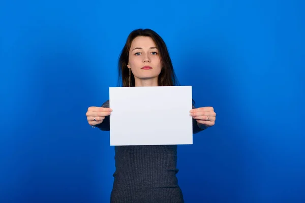 Gri tişörtlü genç bir kadın bir kağıt parçası tutuyor ve kameraya bakıyor, gülümsüyor. Mavi arkaplan izole