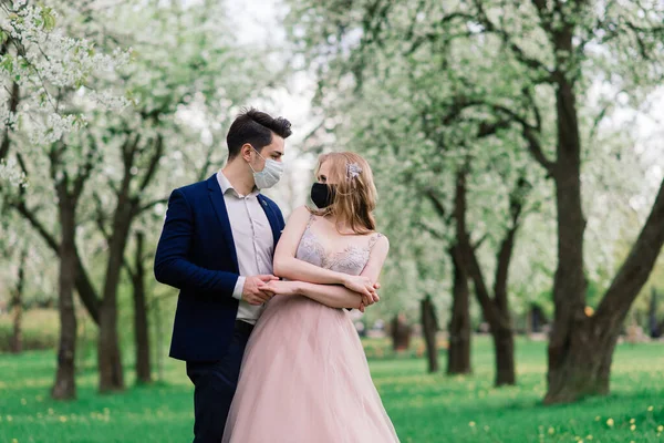 Pareja joven y cariñosa caminando con máscaras médicas en el parque durante la cuarentena el día de su boda. Coronavirus, enfermedad, protección, enfermedad, gripe gripe europa celebración cancelada . —  Fotos de Stock