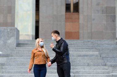 Koruyucu maskeli bir çift, karantina zamanında iş binasının yakınında şehir dışında yürüyüş yapıyor. Coronavirüs kavramı, covid.