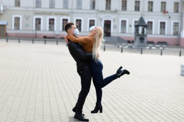 Koruyucu maskeli bir çift, karantina zamanında iş binasının yakınında şehir dışında yürüyüş yapıyor. Koronavirüs salgını..