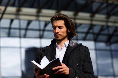 Tam takım elbiseli modern kendine güvenen genç işadamı arka planda şehir manzarasıyla dışarıda duruyor.