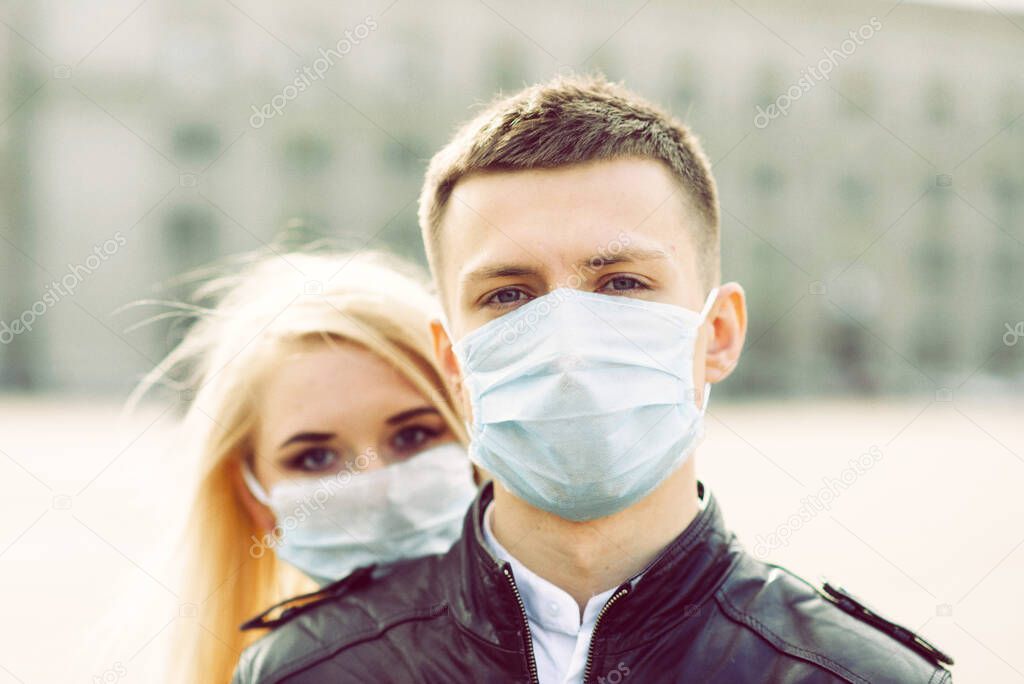 Couple in protective masks have a walk outdoors in the city near business building at quarantine time. Conception of coronavirus, covid.
