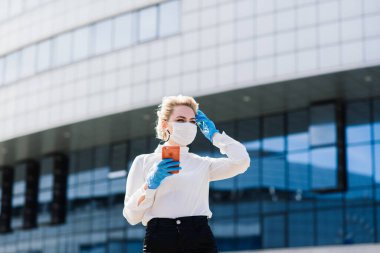 Telefonlu, defterli, tabletli, açık havada kahve içen genç bir iş kadınının portresi. Lastik mavi eldivenli güzel sarışın kız..