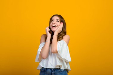 Koyu renk saçlı, gülümseyen ve sarı arka planda poz veren büyük şaşırmış gözleri olan genç bir kadın. Duygusal stüdyo çekimi.