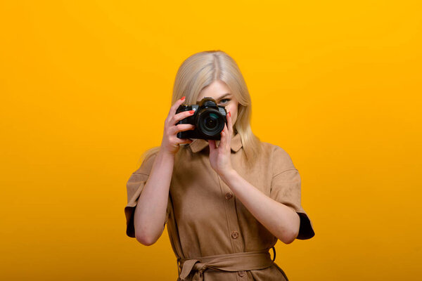 Portrait of a blonde girl with a camera in hand on a yellow background. Isolated studio.
