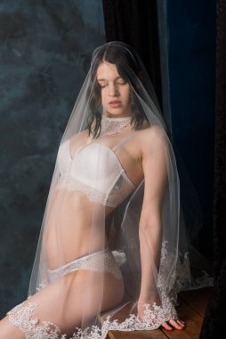 Beyaz iç çamaşırlı güzel gelin yatak odasında ve stüdyosunda oturuyor. Düğün konseptinin sabahı