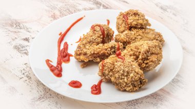 Beyaz bir tabakta bol yağda kızartılmış tavuk ve beyaz arka planda domates ketçapı.