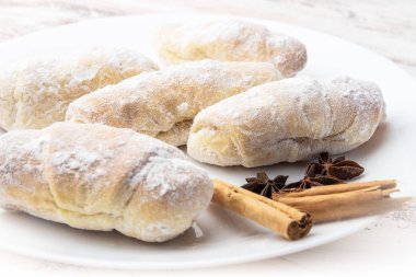 Yiyecek kruvasanları üzerine pudra şekeri serpiştirilmiş tarçın yıldızı anason beyaz bir tabakta hafif bir zemin üzerinde