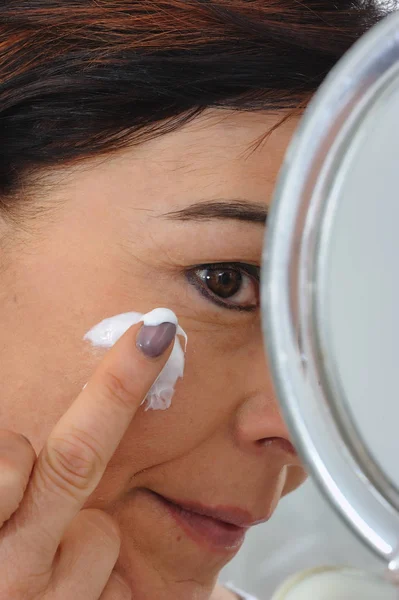 Mature woman puts cream on face — Stock Photo, Image