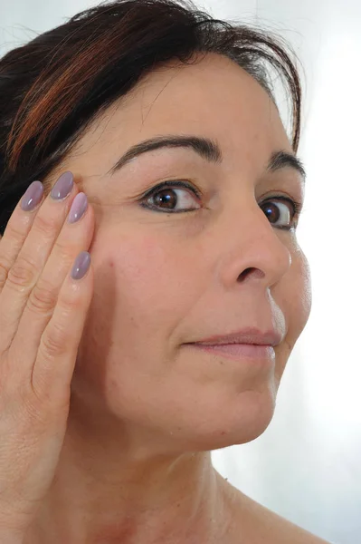 Volwassen vrouw zet crème op gezicht — Stockfoto