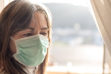 Corona Virüsü. Corona virüsünün hasta kadını pencereden dışarı bakıyor ve güvenli nefes alma koruması takıyor ve evdeki hastalıktan kurtuluyor. Hasta enfeksiyonu önlemek için izole edildi