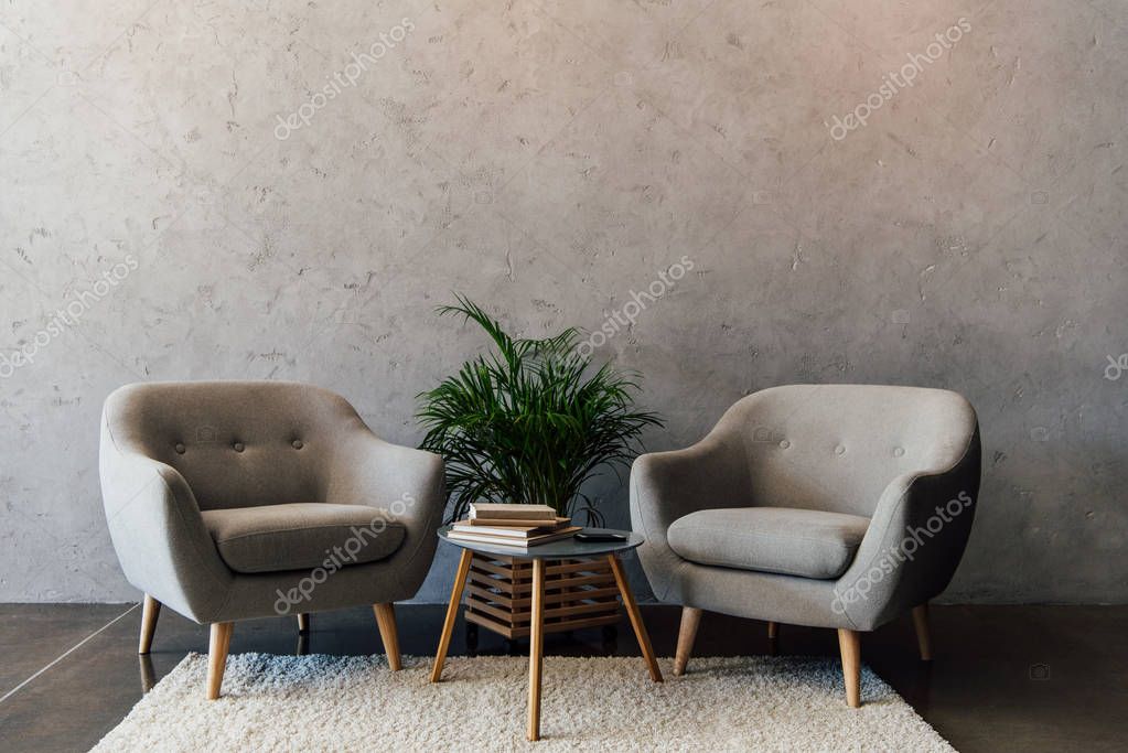 Two cozy grey armchairs standing on white carpet in empty room