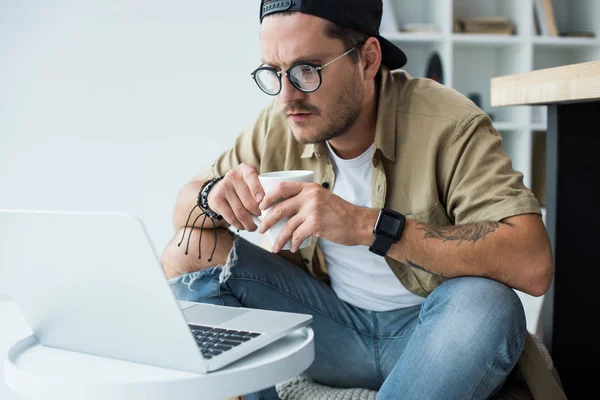Man with cup of coffee looking at laptop — Stock Photo, Image