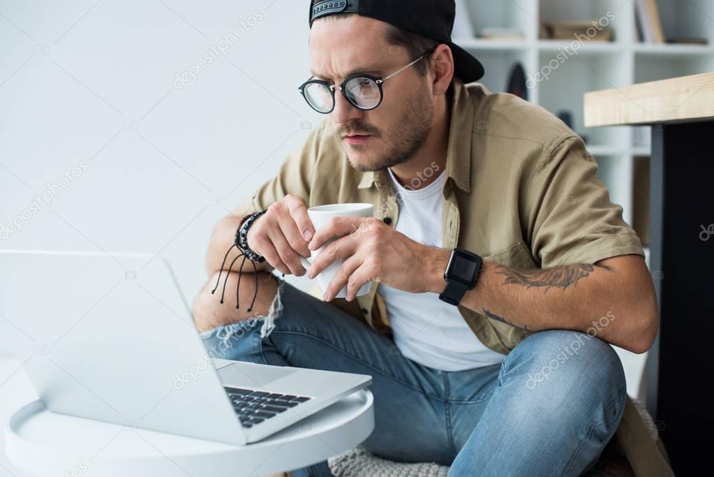 man with cup of coffee looking at laptop