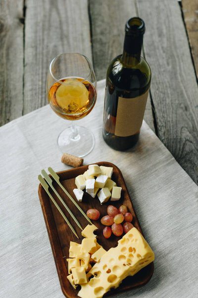 Glass with wine and plate with cheese and grapes