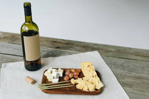 Wine bottle and plate with cheese and grapes — Stock Photo, Image