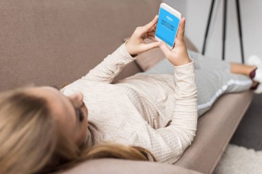 woman on couch using smartphone with skype app on screen clipart