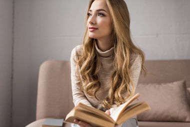 evde rahat kanepede kitap ile düşünceli genç kadın