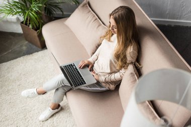 high angle view of young woman working with laptop on sofa clipart