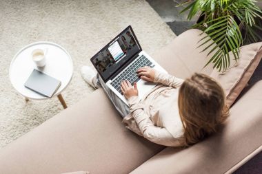 yüksek açılı görünüş kadının evde kanepede oturan ve LinkedIn Web sitesinde ekran ile dizüstü bilgisayar kullanarak