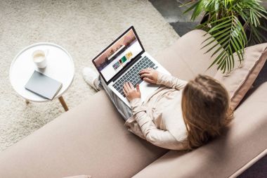 high angle view of woman at home sitting on couch and using laptop with shutterstock website on screen clipart