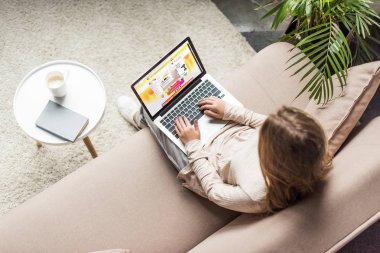 yüksek açılı görünüş kadının evde kanepede oturan ve aliexpress Web sitesinde ekran ile dizüstü bilgisayar kullanarak