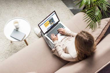 yüksek açılı görünüş kadının evde kanepede oturan ve dizüstü ekran üzerinde rezervasyon Web sitesi ile kullanma