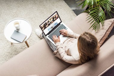 high angle view of woman at home sitting on couch and using laptop with shutterstock homepage on screen clipart