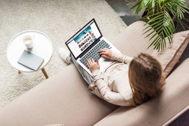 high angle view of woman at home sitting on couch and using laptop with amazon website on screen clipart