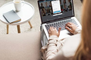 cropped shot of woman at home sitting on couch and using laptop with linkedin website on screen clipart