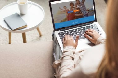 cropped shot of woman at home sitting on couch and using laptop with couchsurfing website homepage on screen clipart