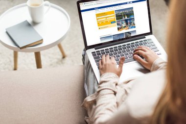 cropped shot of woman at home sitting on couch and using laptop with booking website on screen