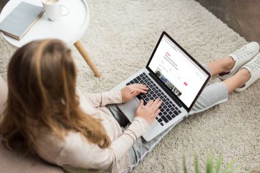 kadının evde yüksek açılı görünüş katta oturan ve airbnb Web sitesinde ekran ile dizüstü bilgisayar kullanarak