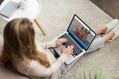 kadının evde yüksek açılı görünüş katta oturan ve dizüstü bilgisayar ekranında couchsurfing Web sitesi ile kullanma