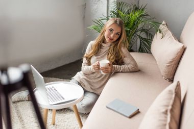 attractive young woman drinking coffee at home while working with laptop clipart