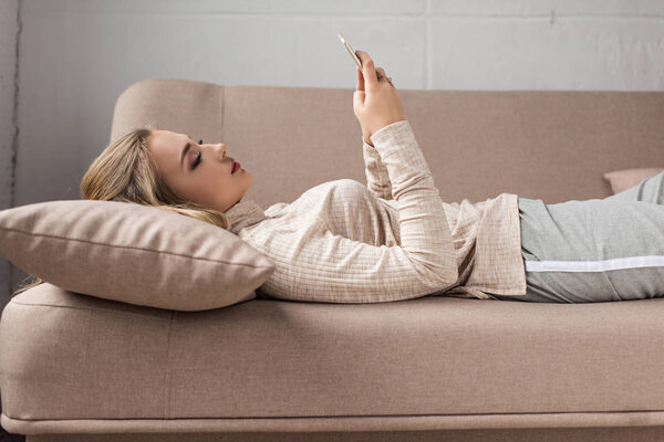 beautiful young woman using smartphone on couch at home