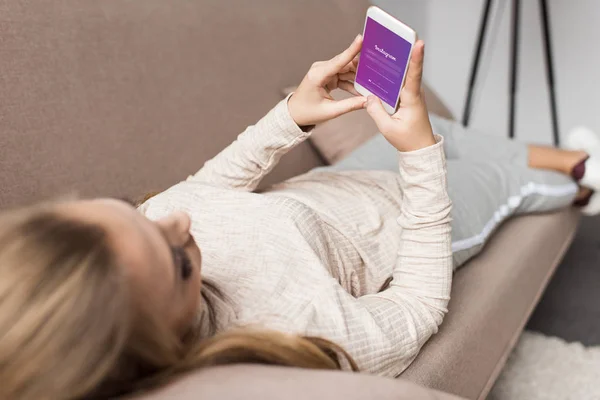 女人在沙发上使用智能手机与 Instagram 应用程序在屏幕上 — 图库照片