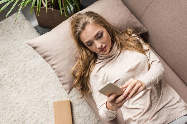 high angle view of young woman using smartphone on couch at home